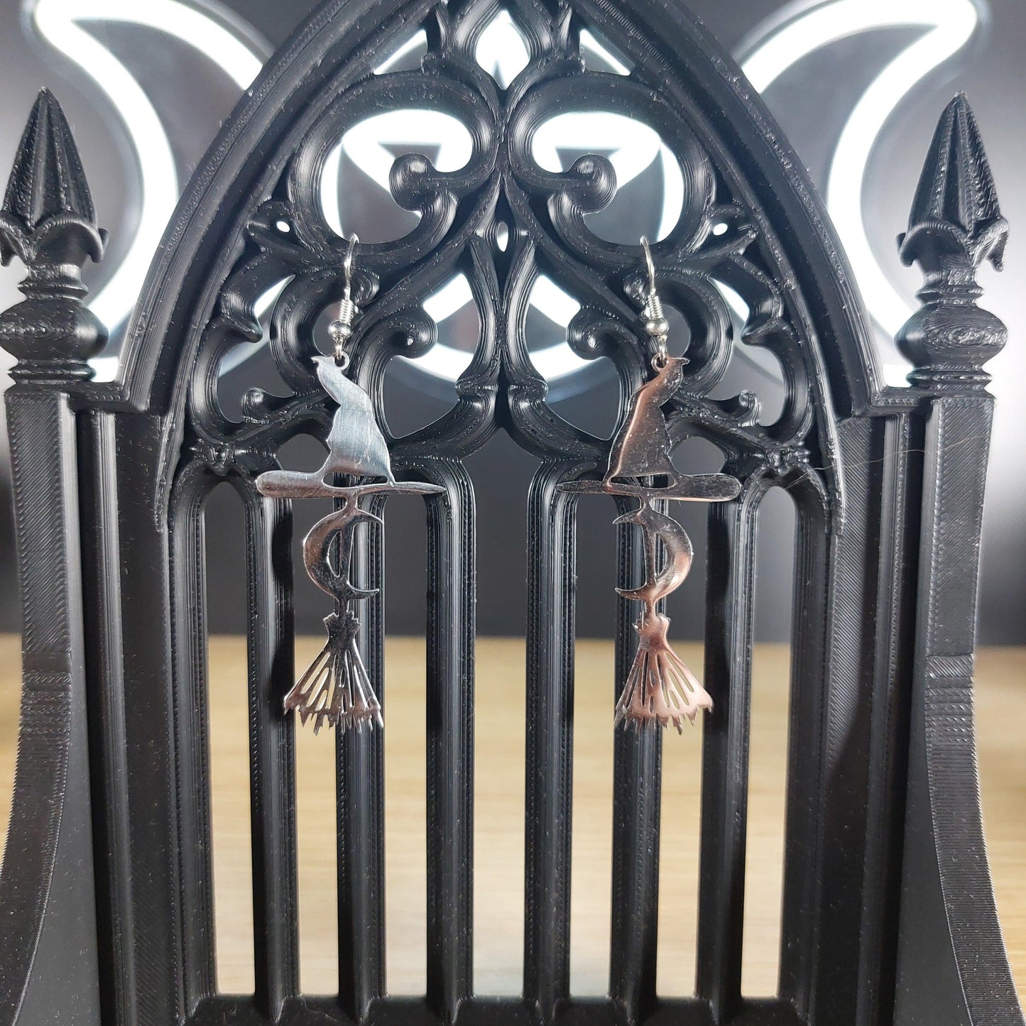 Silver tone broom, witch hat, and crescent moon dangle earrings on a black gothic arch display.