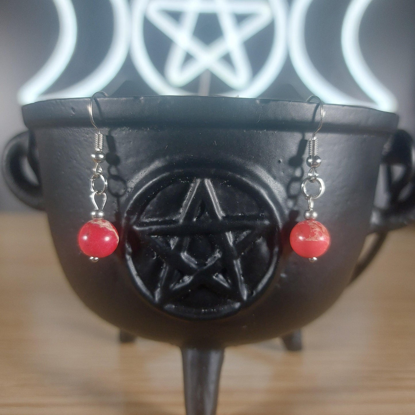 Red jasper crystal beaded dangle earrings with silver hooks, displayed on a black cauldron.