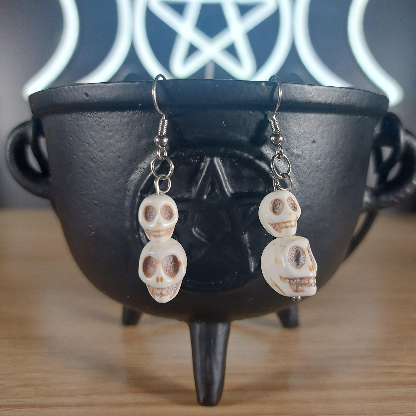 White howlite crystal skull 2-tier dangle earrings on a black cauldron.