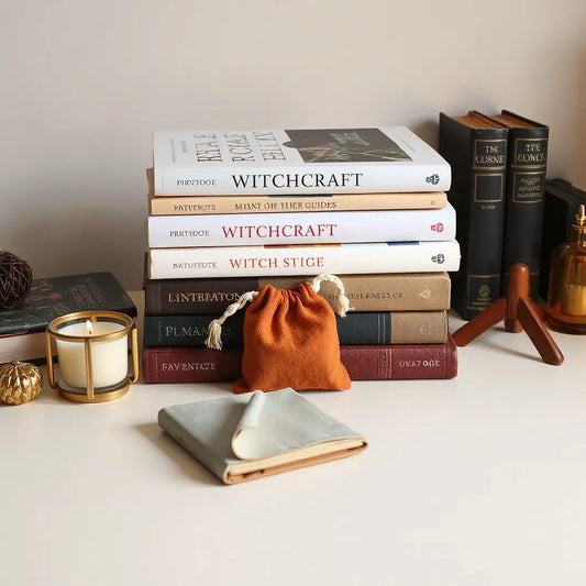 Stacked witchcraft books and guides on a wooden desk with a lit candle and small pouch