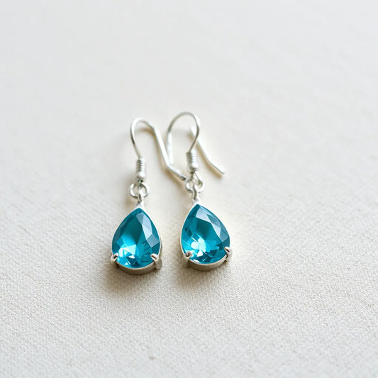 Turquoise crystal earrings with silver hooks on neutral fabric under soft natural light