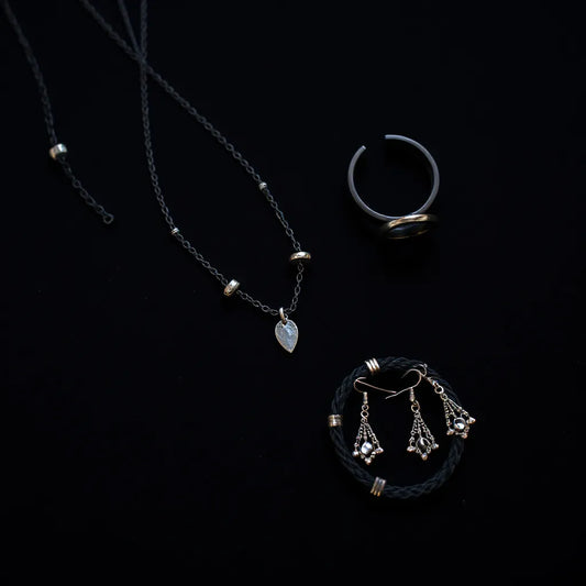 Layered black necklaces with charms, rings, bracelet, and drop earrings on dark velvet