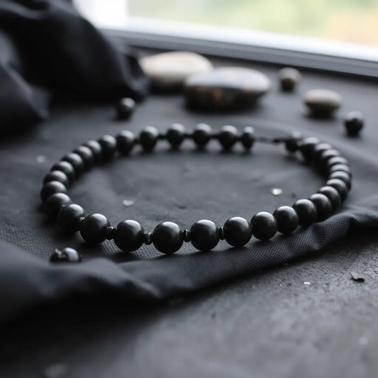 Black obsidian beaded bracelet with glossy beads on dark fabric under soft natural light