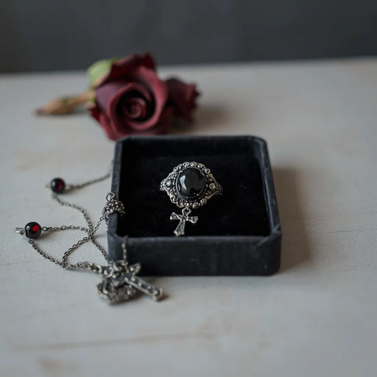 Antique-inspired gothic ring, cross pendant necklace, and dangling earrings on a dark velvet tray
