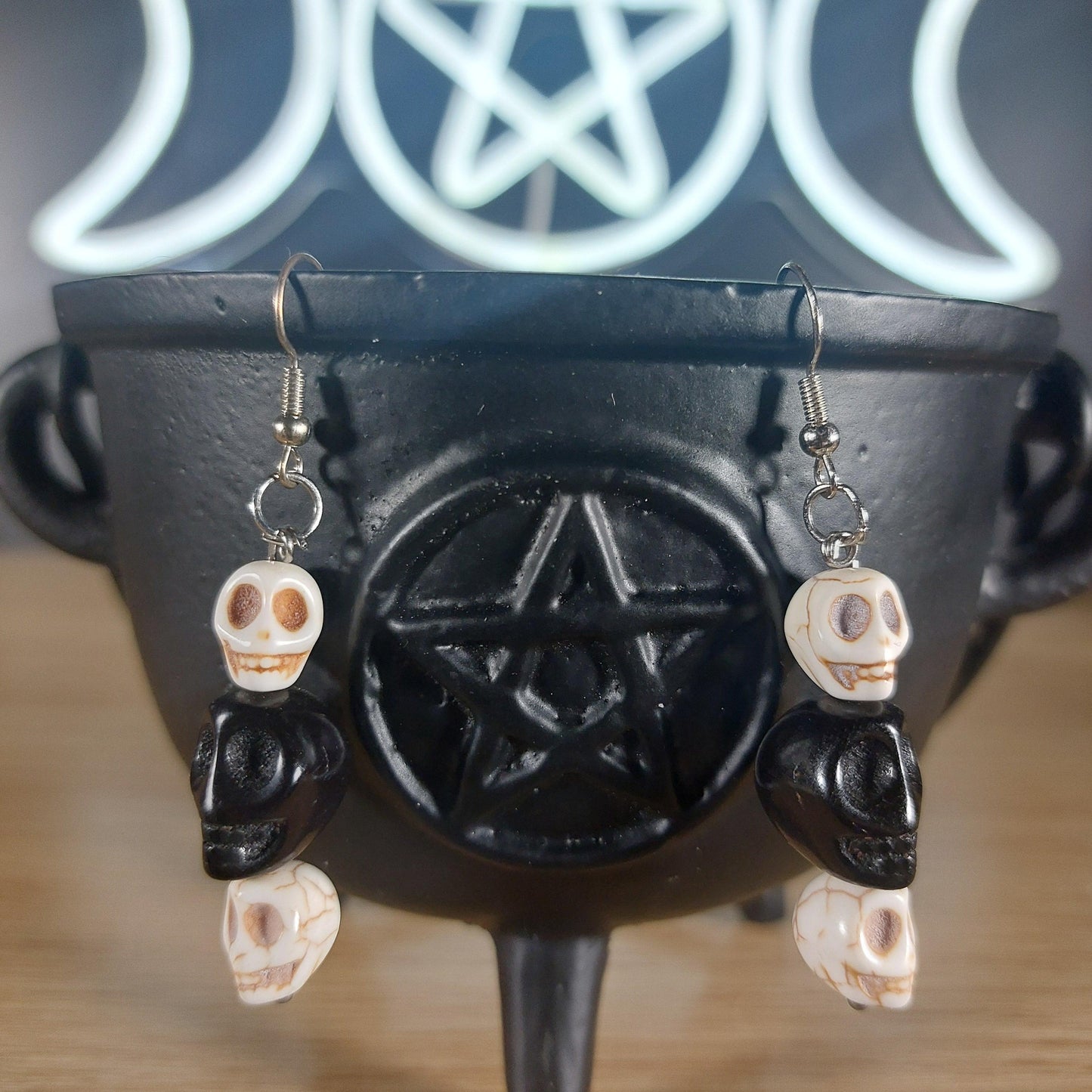 Howlite crystal and black glass skull dangle earrings on a black cauldron.