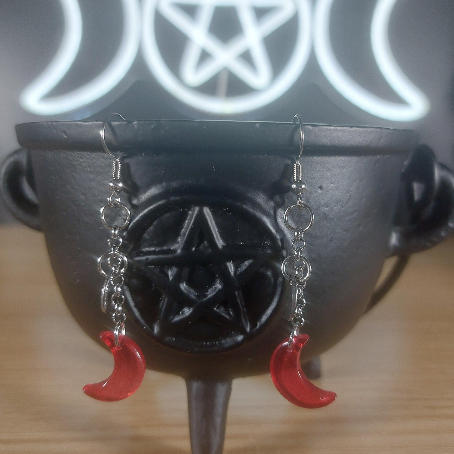 Red glass crescent moon dangle earrings with silver chains, displayed on a black cauldron.