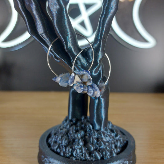 Silver hoop earrings with raw blue sodalite crystal chips, displayed on a dark skeletal hand stand.