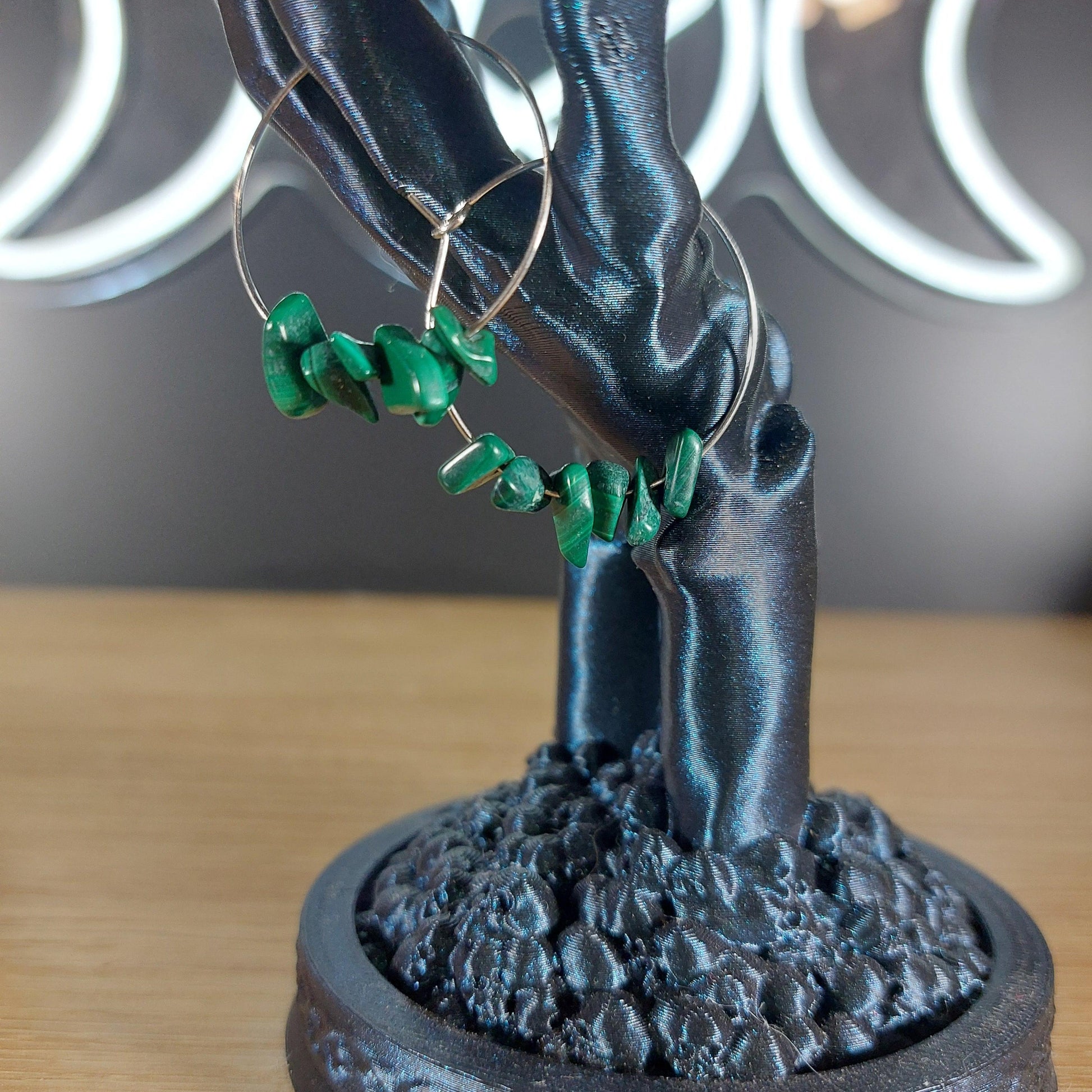 Silver hoop earrings with vibrant green malachite crystal chips on a dark display.