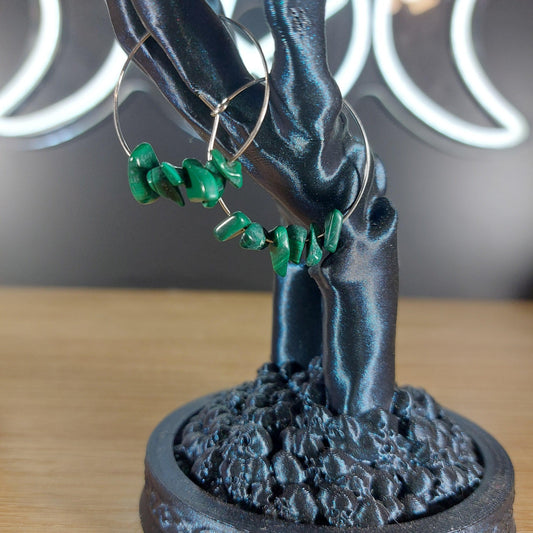 Silver hoop earrings with vibrant green malachite crystal chips on a dark display.