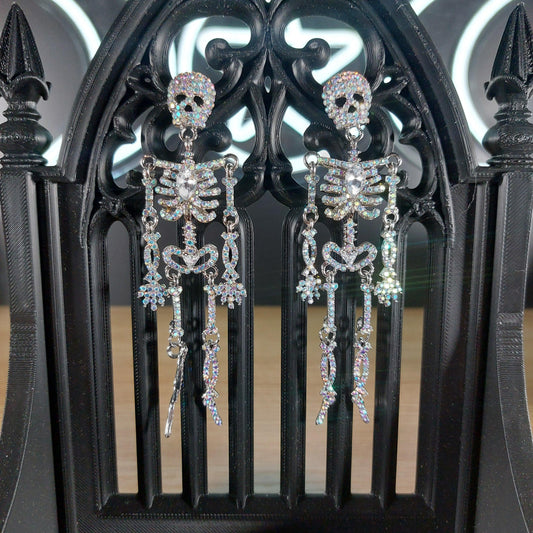 Sparkling rhinestone skeleton dangle earrings on a black gothic stand.