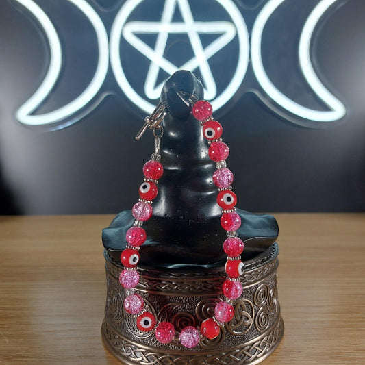 Pink and red glass bead bracelet with evil eye charms and a toggle clasp.