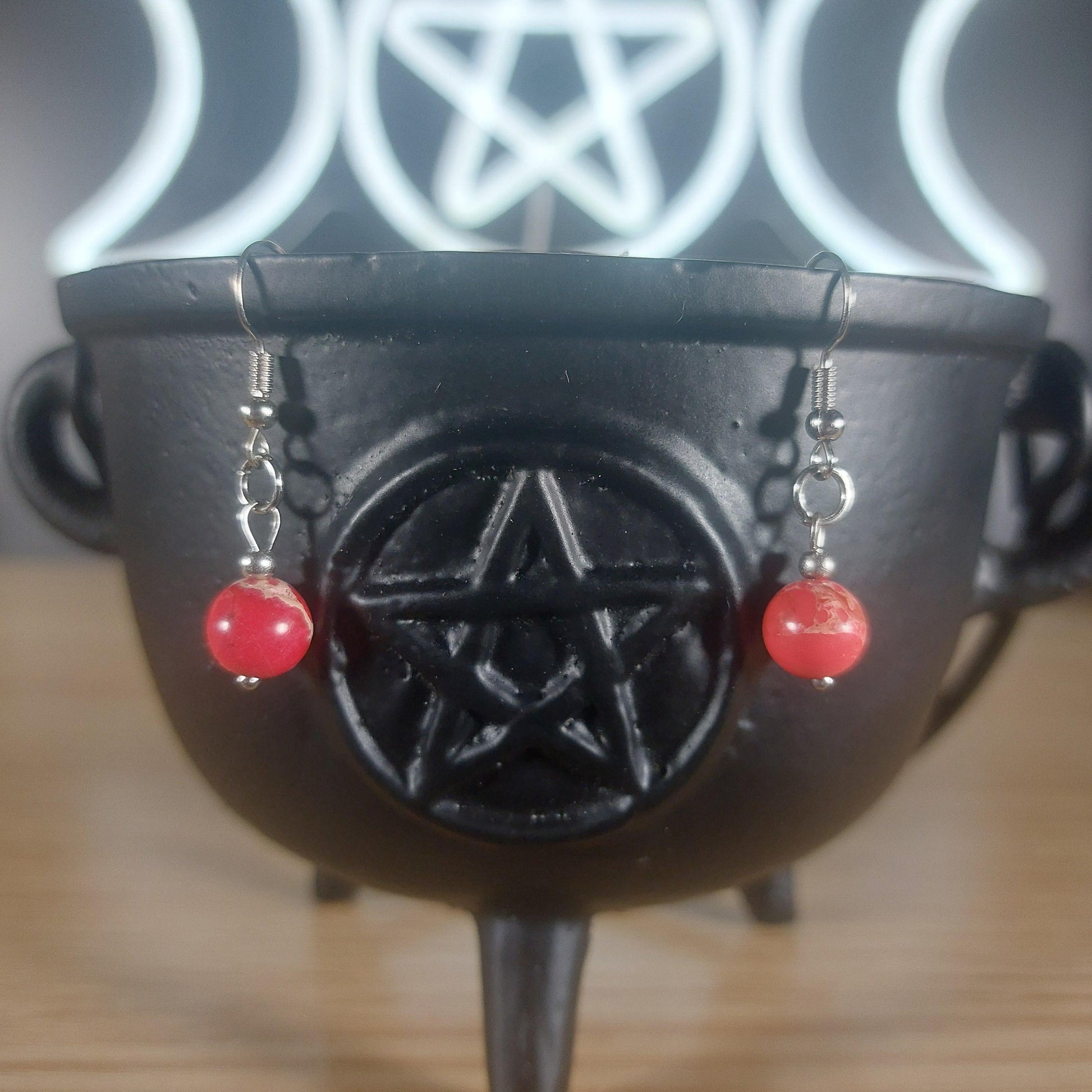 Red jasper crystal beaded dangle earrings with silver hooks, displayed on a black cauldron.