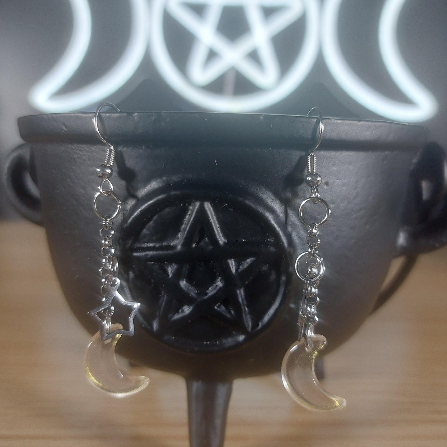 Pale yellow/gold glass moon and silver star dangle earrings on a black cauldron.