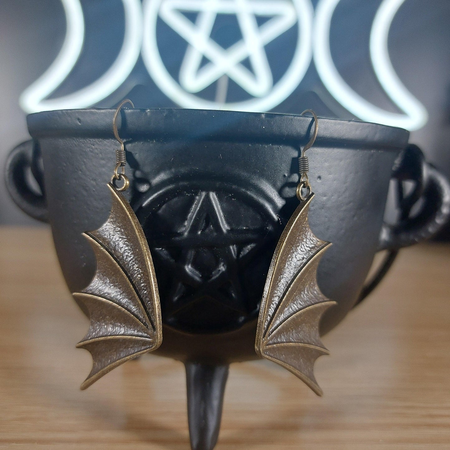 Bronze dragon wing dangle earrings hanging from a black cauldron with a pentagram.