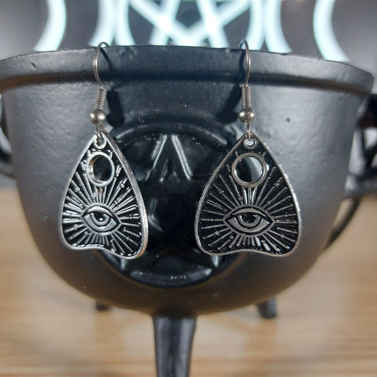 Silver tone evil eye quija planchette dangle earrings hanging from a black cauldron.