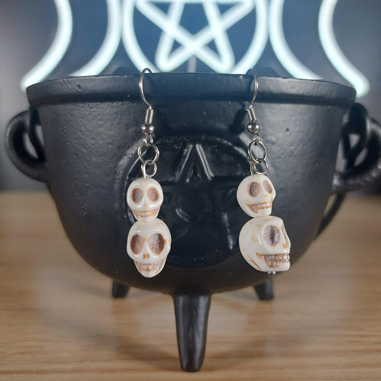 White howlite crystal skull 2-tier dangle earrings on a black cauldron.