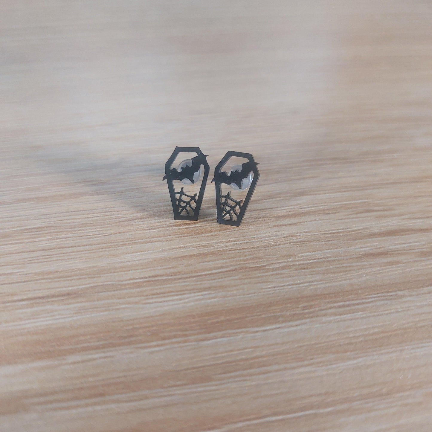 Pair of black coffin stud earrings with bat and spiderweb cutouts.