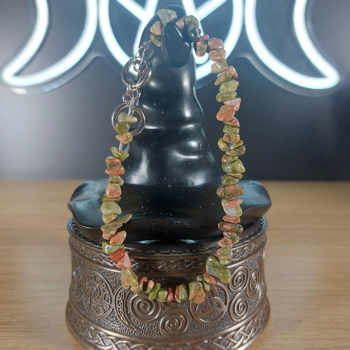 Unakite crystal chip bracelet with green and pink stones, stainless steel toggle clasp, displayed on a black stand.
